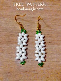 two white and green beaded earrings sitting on top of a wooden table