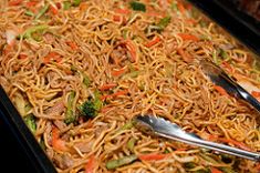 a tray full of noodles and meat with tongs in it, ready to be eaten