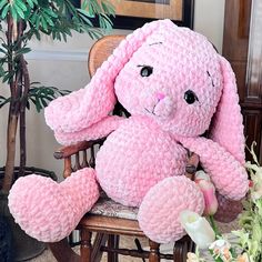 a pink crocheted bunny sitting in a chair next to a potted plant