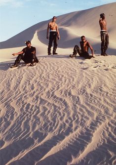 four men sitting on top of a sand dune