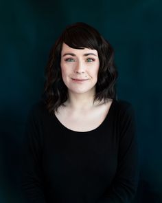 a woman with dark hair and blue eyes smiles at the camera while wearing a black shirt