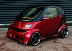 a red smart car is parked in front of a garage door and brick flooring