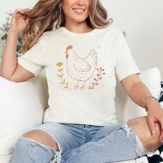 Embrace the charm of the countryside with our rustic chicken and flower shirt. Perfect for nature and animal lovers alike, this tee features a beautifully designed chicken amidst floral elements in a soft, inviting color palette. Made with high-quality materials, it offers both comfort and durability, making it a great addition to any wardrobe. Whether you're layering up for a brisk day or just showing off your love for farm animals, this T-shirt is sure to catch the eye and warm the heart. ☑️ P Country Style Tops With Graphic Print For Spring, Country Style Graphic Print Tops For Spring, Spring Country Style T-shirt With Graphic Print, Country Style Graphic Print T-shirt For Spring, Country Style Short Sleeve T-shirt For Spring, Relaxed Fit Country Tops For Spring, Relaxed Fit Country Style Tops For Spring, Country Style Relaxed Fit Tops For Spring, Cowgirl Top