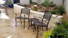 three chairs and a table sitting on a patio next to a planter filled with potted plants