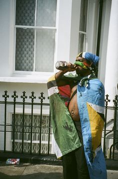 a man standing on the sidewalk with a kite in front of his face and holding a bottle