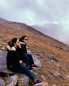 two people sitting on top of a rocky hill