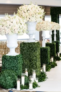 white flowers and greenery are arranged in tall vases at the end of an aisle