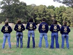 a group of people standing in a field with their back to the camera wearing police shirts