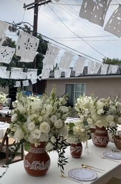 white flowers are in vases on a table with plates and napkins hanging from the clothesline