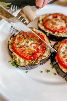 someone is cutting into an eggplant dish on a plate with a fork and knife