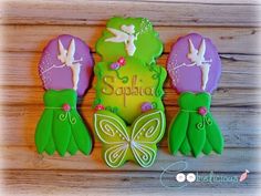 three decorated cookies sitting on top of a wooden table next to some flowers and butterflies