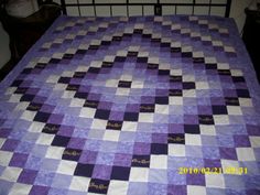 a bed with a purple and white quilt on it