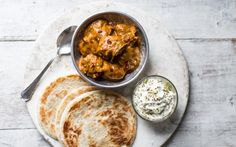 some food is on a white plate with silver spoons and a small bowl filled with sauce