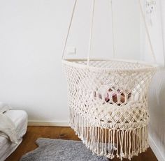 a white macrame hanging on the wall next to a gray rug and pillow