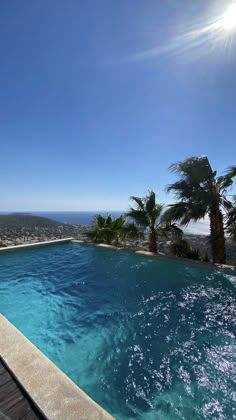 an empty swimming pool with palm trees and the sun shining over the ocean in the background