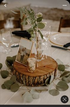 a wooden table topped with a vase filled with flowers and greenery next to pictures