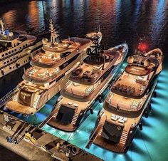 several yachts are docked in the water near each other and one is lit up at night