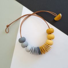 a necklace with yellow, grey and white beads on a brown cord next to an earphone