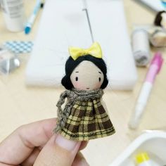 a small doll is being held up by someone's hand on a table with other crafting supplies