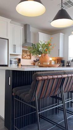 a kitchen with three lights hanging from the ceiling and two bar stools in front of it