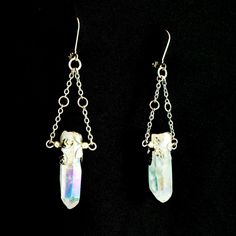 These beautiful angel aura quartz earrings are a dazzling addition to your jewelry collection. The rainbow glimmer on the crystal shimmers as the light catches it at different angles. Each crystal has two hand molded flower charms that wrap around the crystal and the silver finish give them an elegant yet bold feel. These are real gemstone earrings that dangle and have some weight to them. These earrings are not for those who are sensitive to heavily weighted earrings, but if you like to flaunt Iridescent Pierced Drop Earrings, Iridescent Sterling Silver Dangle Earrings, Handmade Mystical Crystal Jewelry, Handmade Ethereal Dangle Jewelry, Ethereal Handmade Dangle Jewelry, Silver Crystal Earrings With Gemstones, Handmade Silver Crystal, Iridescent Dangle Crystal Earrings For Pierced Ears, Mystical Silver Drop Earrings