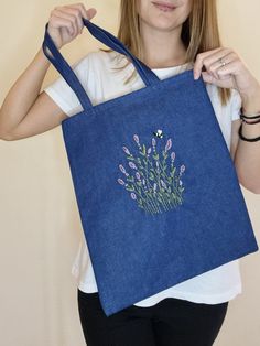 a woman holding up a blue bag with flowers on the front and bottom part of it