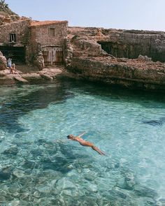 a man swimming in clear blue water next to an old stone building on the shore