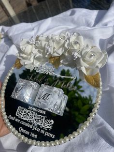 a person holding up a glass plaque with flowers and pearls on it's side