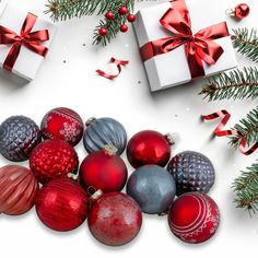 christmas ornaments and presents on a white surface with red ribbon, pine branches and bows