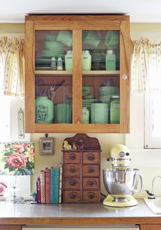 an old fashioned kitchen with wooden cabinets and green dishes on the counter top in front of it