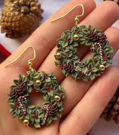 a pair of christmas wreath earrings with candy canes and holly leaves on them, sitting in someone's hand