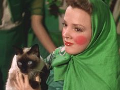 a woman in green holding a siamese cat