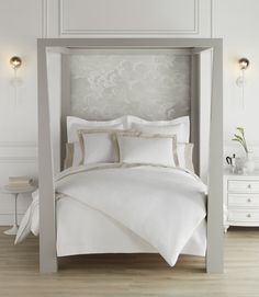 a bed with white linens and pillows in a large room, surrounded by wall sconces