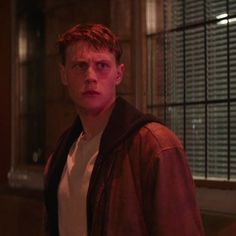 a young man standing in front of a window with blinds on the windowsills