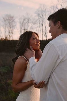 a man and woman standing next to each other in a field with trees behind them