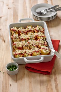 a white casserole dish filled with stuffed shells and sauce on a red napkin