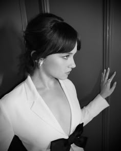 a woman in a white jacket and black bow tie looking at her hand on the wall