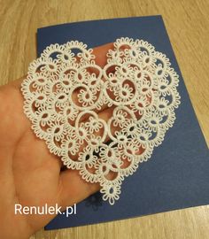 a hand holding a heart shaped doily on top of a blue card