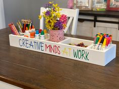 a wooden desk with markers, pencils and pens in a container on it that says creative minds at work