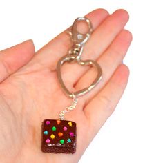 a hand holding a small square shaped chocolate keychain with sprinkles