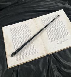 an open book with a harry potter wand laying on it's side next to a pen