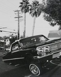 an old black and white photo of a car driving down the street with palm trees in the background