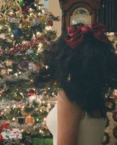 a woman with long hair wearing a red bow around her neck in front of a christmas tree