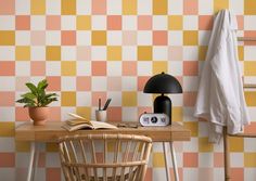 a desk with a lamp, book and potted plant on it in front of a checkered wall