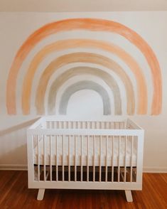 a white crib in front of a wall with a rainbow painted on it's side