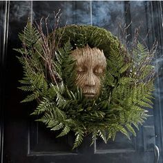 a wreath with a face made out of leaves and branches on the front door to a house