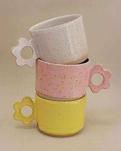 three cups stacked on top of each other in different colors and shapes, one with a flower decoration