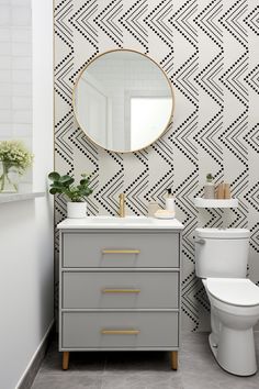 a white toilet sitting next to a sink in a bathroom under a large round mirror