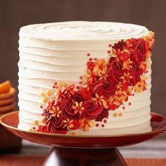 a white cake with red and orange flowers on it sitting on a wooden table next to crackers