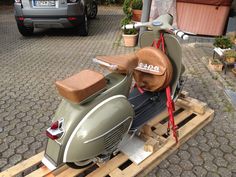 a green scooter with a wooden seat on a pallet in front of a car